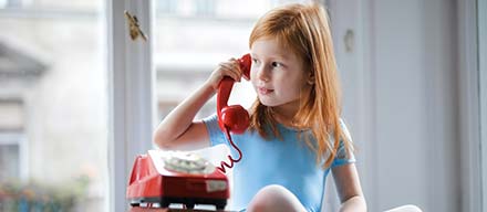 Liten flicka som pratar i en röd fast telefon