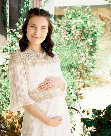 Gravid kvinna i vit klänning med blommande buske i bakgrunden